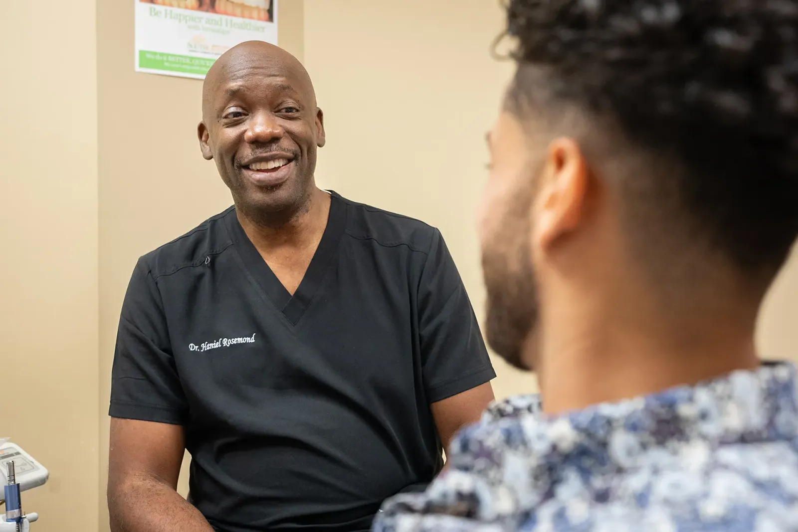 Dr. Haniel Rosemond talking with an adult patient beneath an Invisalign poster
